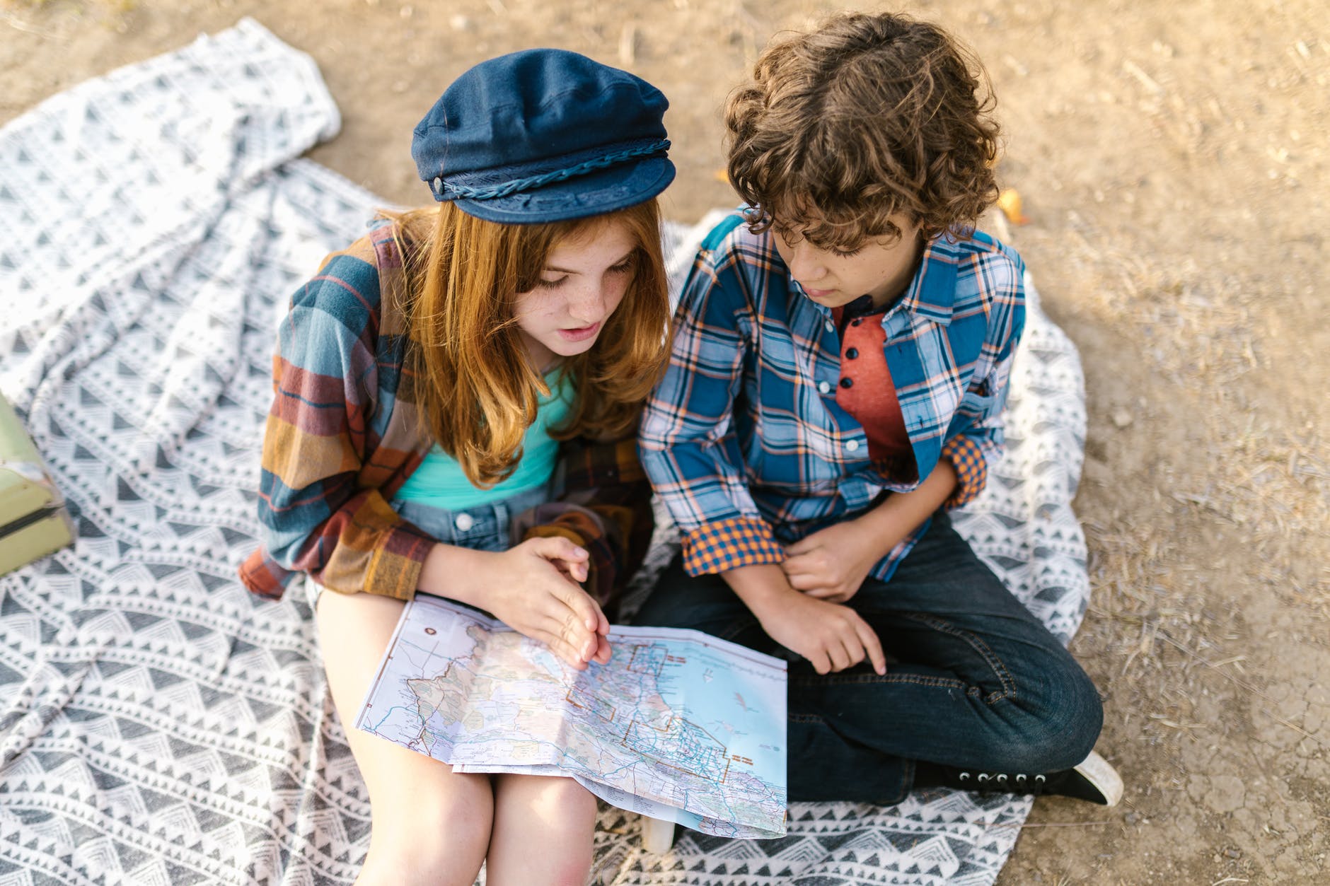 overhead shot of two kids sitting on picnic blanket while looking at a map